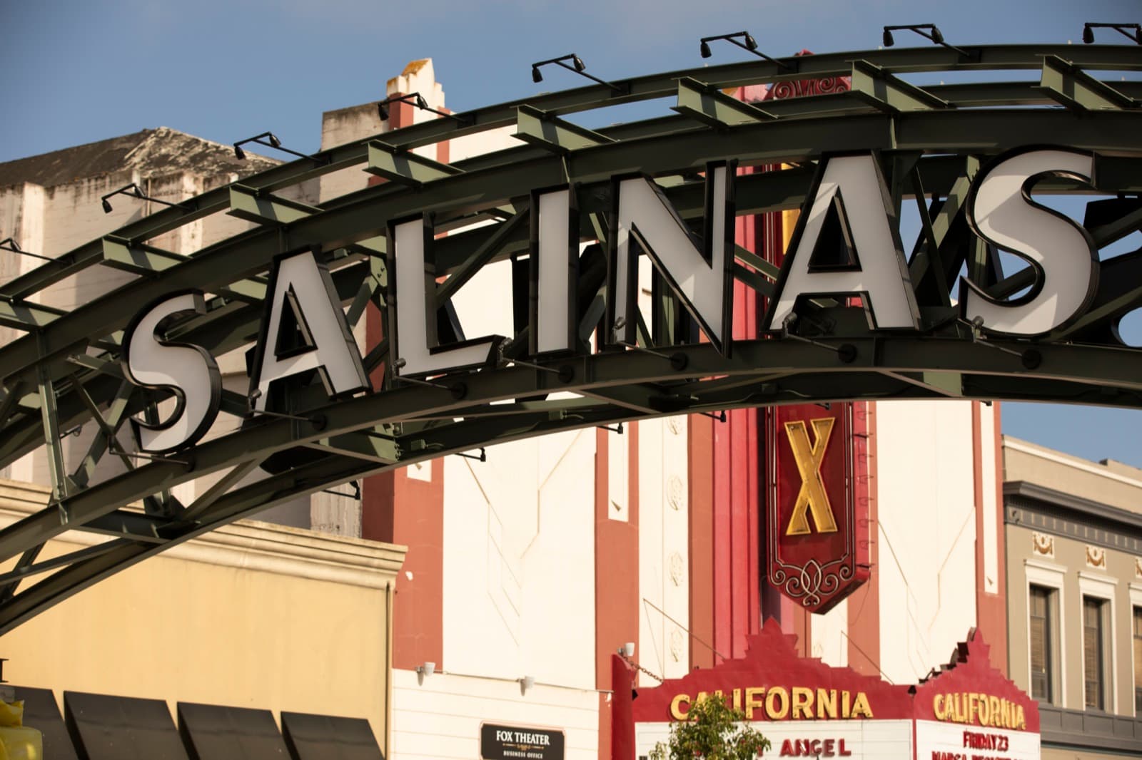 The Salinas arch over Main Street in downtown Salinas at golden hour, with the Fox California Theatre’s vertical blade sign and its CALIFORNIA marquee behind it