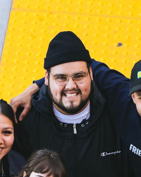 Francisco, who runs Salinas Marketing: a portrait in a black beanie and glasses, wearing a Champion jacket, against a yellow tactile paving wall